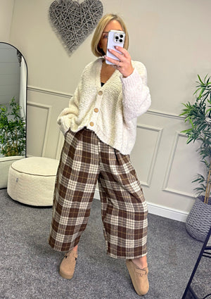 Person wearing a white cardigan and plaid pants taking a mirror selfie.