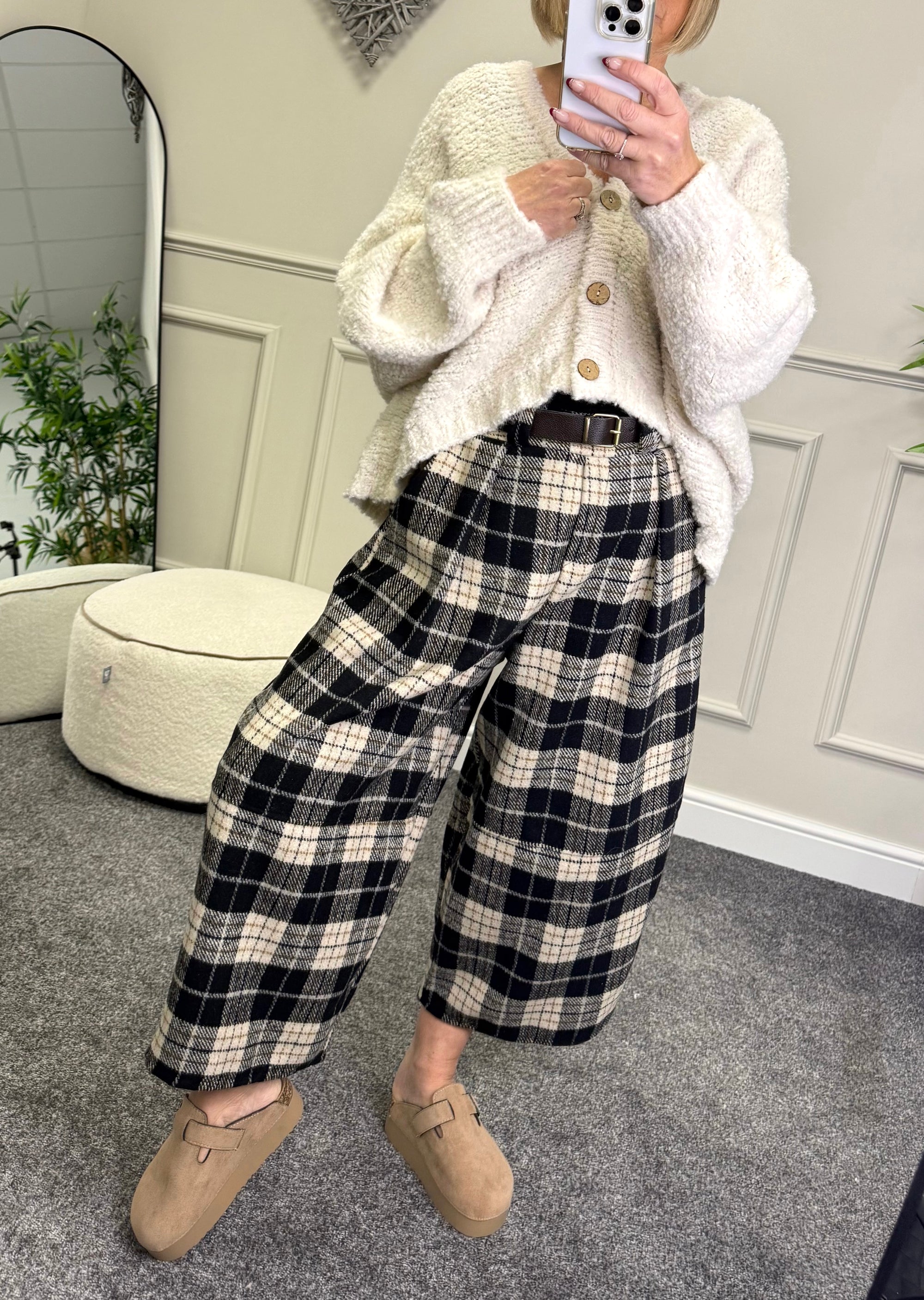 Person wearing a white textured sweater and black and white plaid pants, standing in a room.