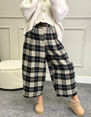 Person wearing black and white plaid pants with a white cardigan in a room.