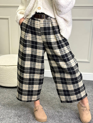 Person wearing black and white plaid pants with a white coat and beige shoes.