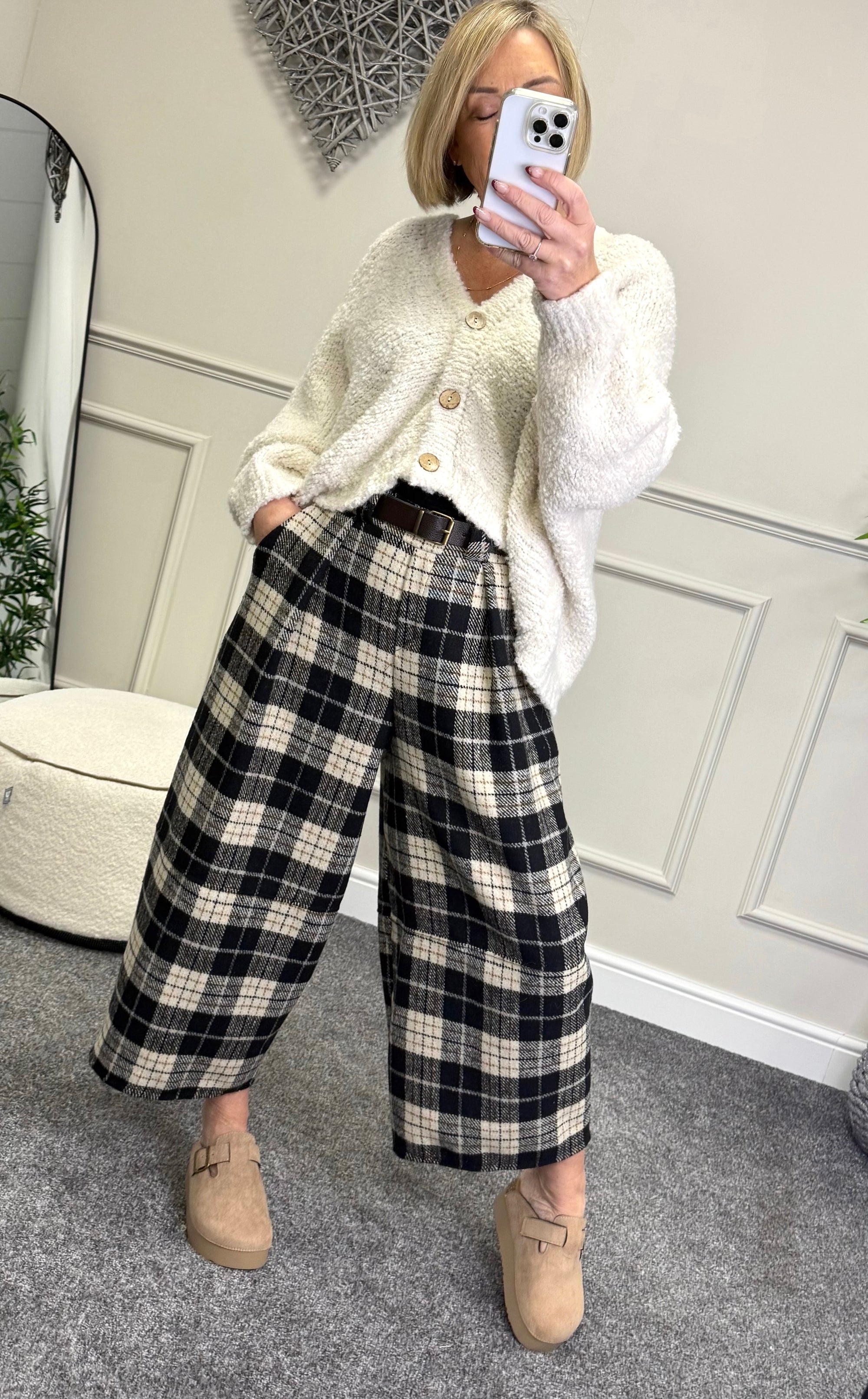 Person wearing a white cardigan and plaid pants taking a mirror selfie.