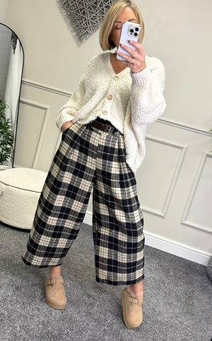 Person wearing a white cardigan and plaid pants taking a mirror selfie.