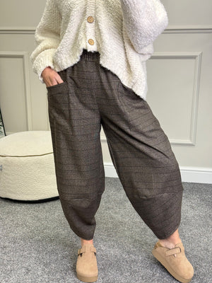 Person wearing brown checkered pants and a white cardigan in an indoor setting.