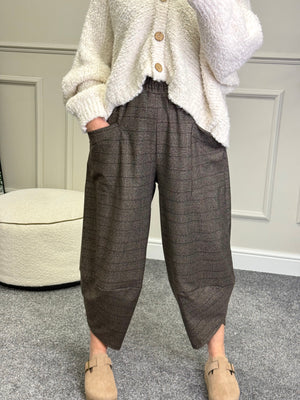 Person wearing a white cardigan and brown plaid pants standing in a room with a neutral background.