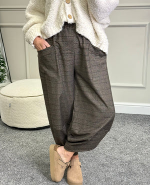 Person wearing a white cardigan, chocolate checkered pants, and beige shoes indoors.