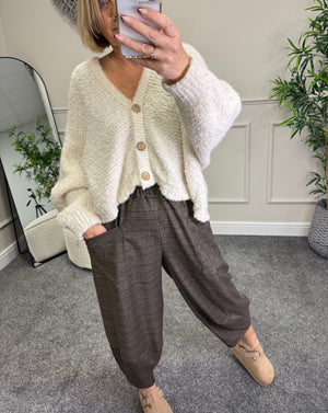 Person wearing a cream cardigan and brown pants taking a mirror selfie.